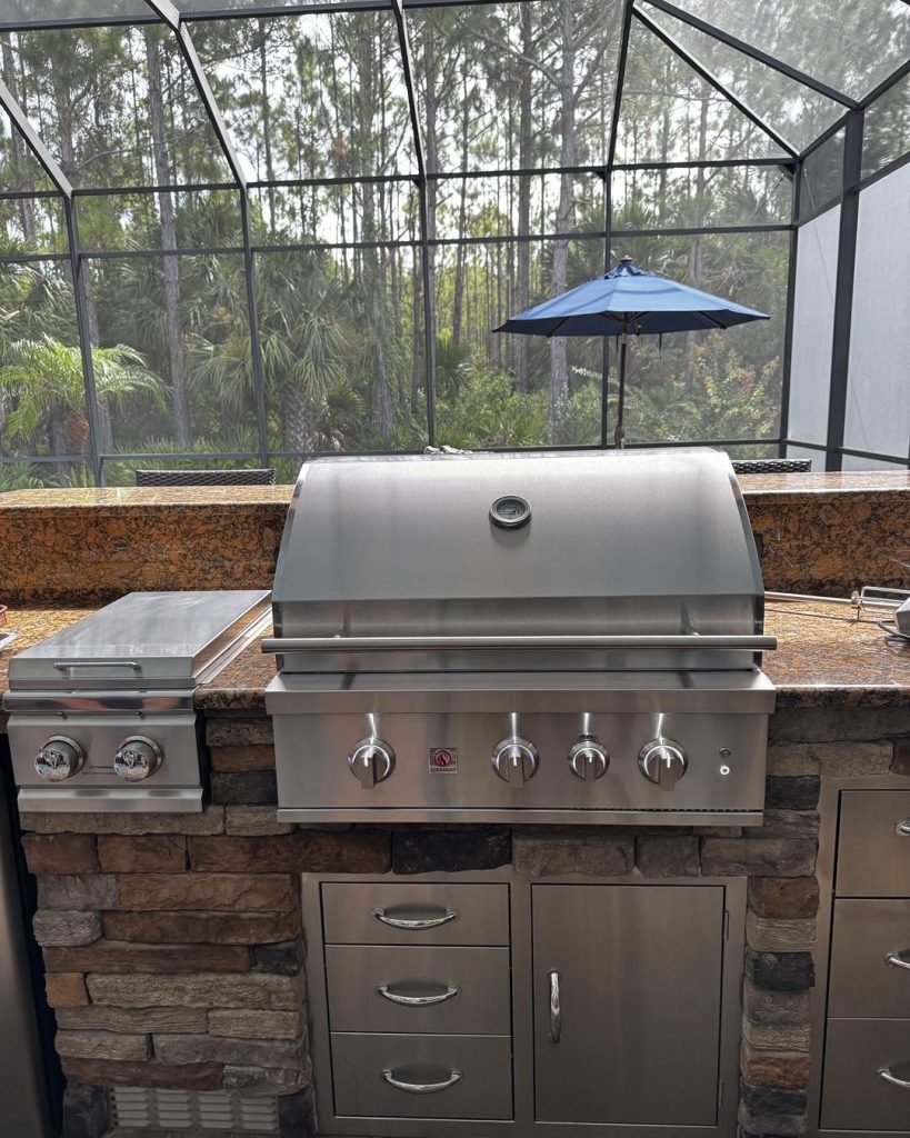 New built-in stainless gas grill in a stone outdoor kitchen island inside a screened Florida pool cage