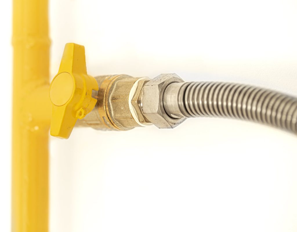 Quarter-turn gas shutoff valve with a yellow handle joining a gas pipe to a flexible stainless steel appliance connector