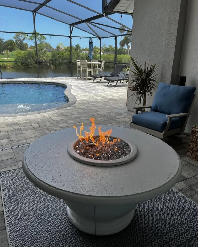Round gas fire table beside a pool on a screened lanai